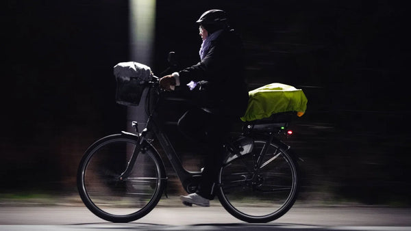Cycliste roulant de nuit avec des bagages sur le porte-bagages et un feu arrière rouge visible.