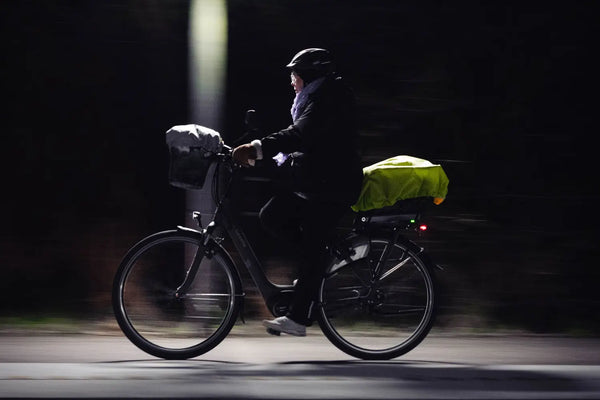 Cycliste roulant de nuit avec des bagages sur le porte-bagages et un feu arrière rouge visible.